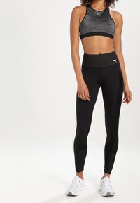 Leggings neri a vita alta con reggiseno sportivo grigio texturizzato con rifiniture nere. Il modello indossa scarpe da ginnastica bianche. Design semplice.