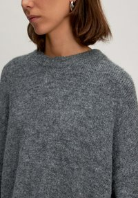 Grauer gestrickter Pullover mit Rundhalsausschnitt, weicher Textur und lockerer Passform. Enthält lange Ärmel und ein dezentes meliertes Muster.