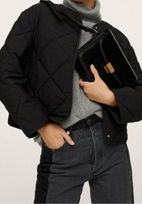 Veste matelassée noire avec boutons-pression, col roulé en maille grise, et sac à main noir avec ferrures dorées. Associés à un jean foncé.