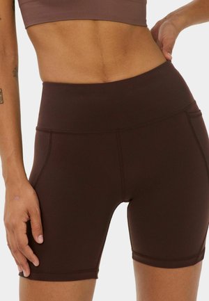 Close-up of a person wearing high-waist dark brown fitted biker shorts and a matching cropped top against a plain background.