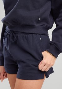 Navy blue shorts made of soft fabric with an elastic waistband and drawstring. Features side pockets and small brand label on the waistband.