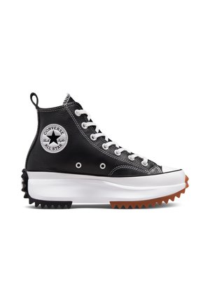 Black leather high-top Converse sneaker with white laces, thick white sole, and jagged black and brown tread.