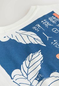 Fehér szöveten kék téglalap alakú mintázat fehér levélillusztrációkkal és fehér stilizált szöveggel egy ázsiai írásrendszerben.