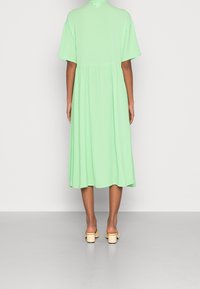 Mintunvihreä midimekko, jossa on lyhyet hihat, laskostettu vyötärö ja liehuva helma. Yhdistetty beigen värisiin lohkopiikkikorkoisiin sandaaleihin. Sileä, kevyt kangas.