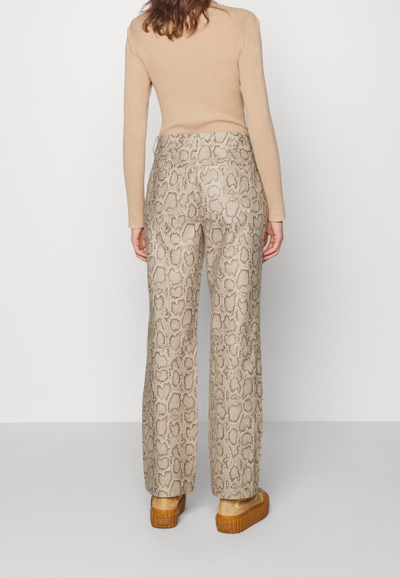 Un haut beige à rayures et à manches longues associé à un pantalon marron clair avec un motif de peau de serpent, avec une coupe droite et des chaussures à plateforme.
