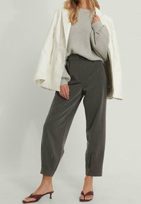 Maglione grigio lavorato a maglia, giacca bianca in ecopelle, pantaloni verdi scuri a vita alta e sandali con tacco marroni. Tessuti texturizzati e vestibilità comoda.