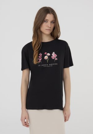 T-shirt di cotone nero con un design floreale in rosa e bianco, con il testo "LE JARDIN PARISIEN" sotto. Maniche corte e fit rilassato.