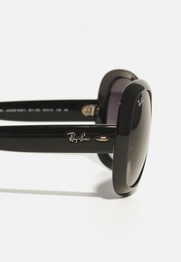 Ochelari de soare Ray-Ban negri cu ramă pătrată, lentile închise la culoare și detalii din metal auriu pe brațe. Textură din plastic neted.
