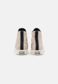 Baskets hautes beiges en toile avec des accents à rayures noires. Dotées d'une semelle en caoutchouc et du logo Converse All Star à l'arrière.