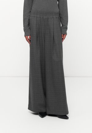 Pantalones grises de piernas anchas con un patrón de cuadros negros, combinados con una camiseta de manga larga gris oscuro y zapatos negros de punta estrecha.