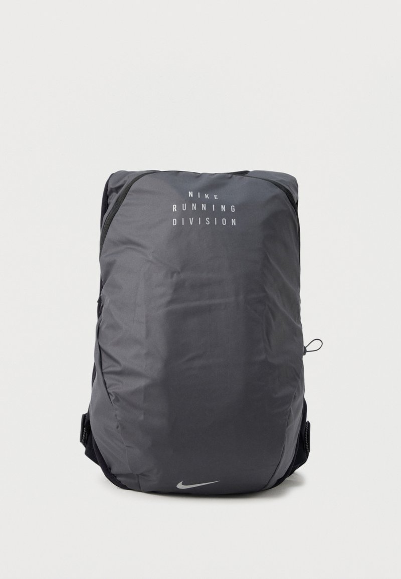 Sac à dos noir Nike Running Division avec logo et texte blancs, posé debout sur un fond blanc uni.