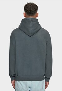 Mørkegrå hættebluse med afslappet pasform, blød tekstur og ribbede manchetter. Har en kængurulomme og minimale syninger.