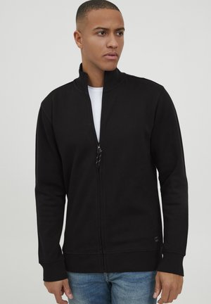Black zip-up sweatshirt with a high collar, long sleeves, and ribbed cuffs, made from a soft fabric. Features a small logo near the hem.