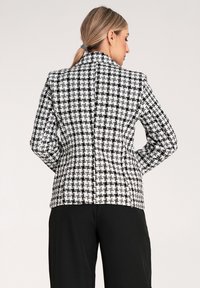 Marynarka w czarno-białą kratę z dopasowanym krojem, wyraźnymi ramionami i gładkim wykończeniem. Widok z tyłu, z widocznymi szwami.