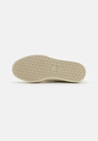 Semelle d'une chaussure avec un motif en nid d'abeille, de couleur beige et surface texturée pour l'adhérence. Logo embossé sur le côté.