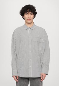 Chemise à rayures avec col, rayures verticales noires et blanches, manches longues, coupe décontractée et détail d'une poche avant sur le côté gauche.