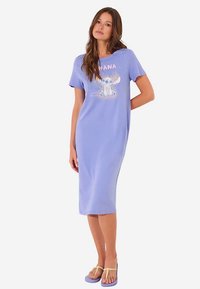 Ljuslila kortärmad klänning i mjukt material med ett motiv av en karaktär och texten "OHANA" i rosa, knälång.