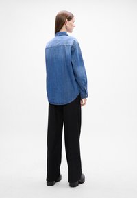 Camicia di jeans, blu, maniche lunghe, polsini a bottoni, orlo curvo, abbinata a pantaloni larghi neri e scarpe nere chunky.