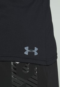 Černé sportovní tričko se světle šedým logem Under Armour v dolním levém rohu. Tričko má hladkou texturu a krátké rukávy.