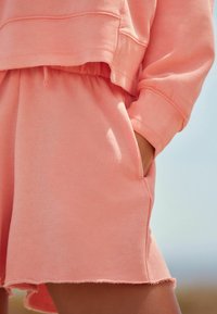 Lys rosa, cropped sweatshirt med rund nederkant og ribbede manchetter, parret med matchende shorts med rå nederkant og sidelommer.