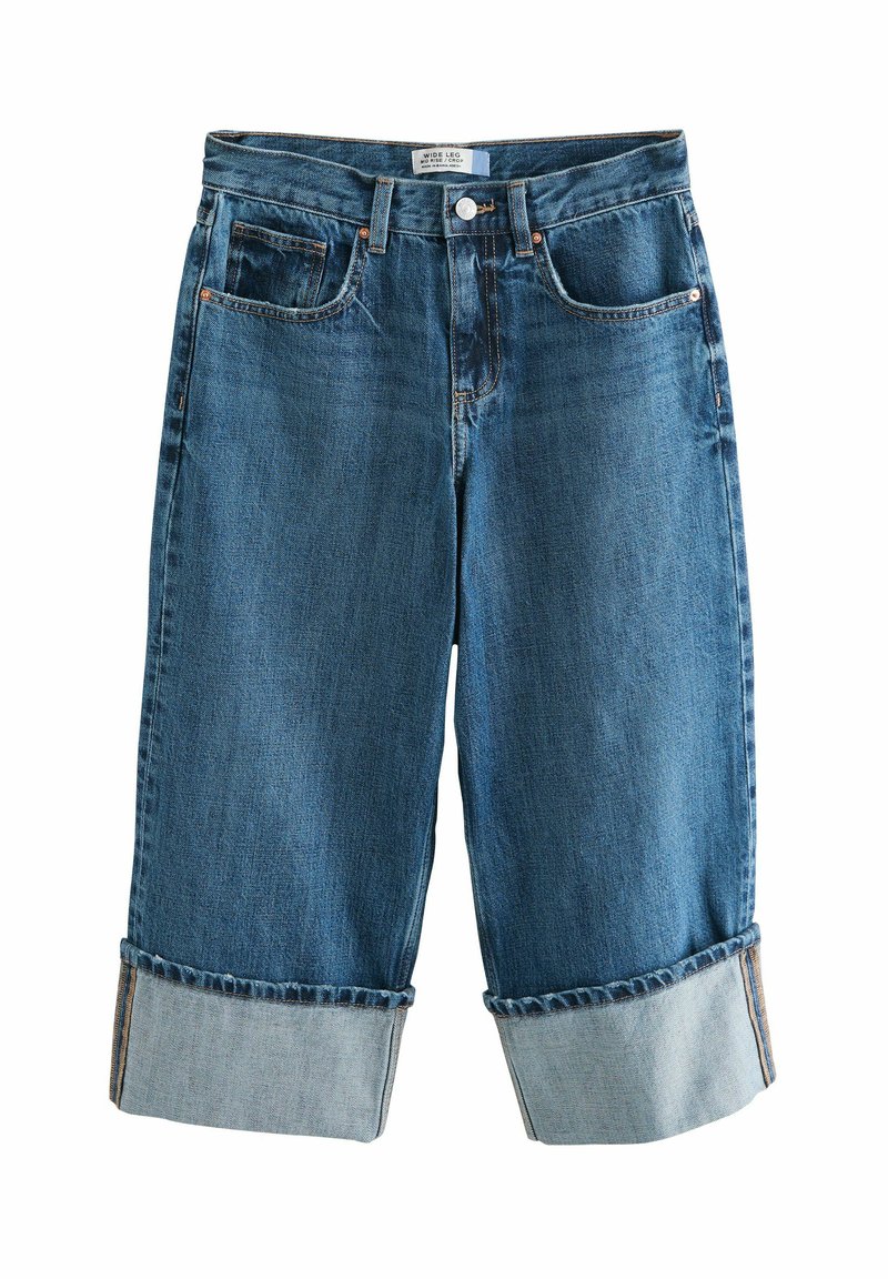 Wijdvallende denimshorts in donkerblauw, met opgerolde manchetten, voor- en achterzakken, en koperen hardware zichtbaar in de taille.