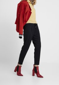 Roter Zip-Up Hoodie, gestreifter Rollkragenpullover in Gelb und Weiß, schwarze tapered Pants und rote blockierte Knöchelstiefel mit schwarzen Seitenpanelen.
