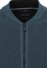 Bomull zip-up kofta i mörk teal med en strukturerad väv, ribbad krage och svart dragkedja. Varumärkesetikett synlig inuti.