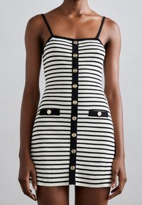 Robe à rayures noires et blanches avec une coupe ajustée, dotée d'une patte de boutonnage à l'avant, de deux poches noires et de fines bretelles. Texture côtelée.