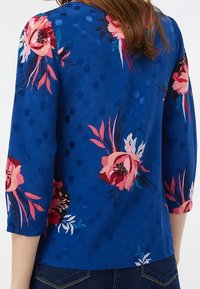 Top a fantasia floreale blu con fiori rosa e bianchi. Presenta scollatura tonda, maniche a tre quarti e motivo a pois testurizzati.