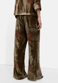 Aksamitne spodnie piżamowe w oliwkowej zieleni, z wzorem drzew w głębokiej czerwieni. Rozszerzany fason z miękką teksturą i luźnym krojem.