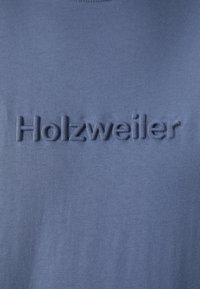 T-shirt in cotone blu con la scritta in rilievo "Holzweiler" al centro. Tessuto liscio, scollatura rotonda e vestibilità rilassata.