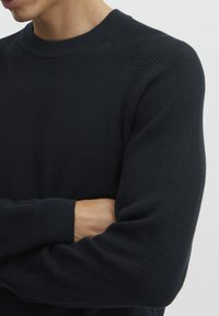 Pulover tricotat de culoare bleumarin închis, cu textură în dungi, guler rotund și mâneci raglan, având o siluetă ajustată. Material moale și elastic.