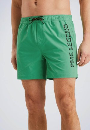 Groene zwembroek met een elastische tailleband en zwarte opdruk aan de zijkant. Het materiaal lijkt licht en soepel te zijn.