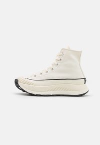 Visoke tenisice od off-white platna s crnom gumom. Značajke uključuju srebrne rupice, vezice i teksturirani akcent na prstima.