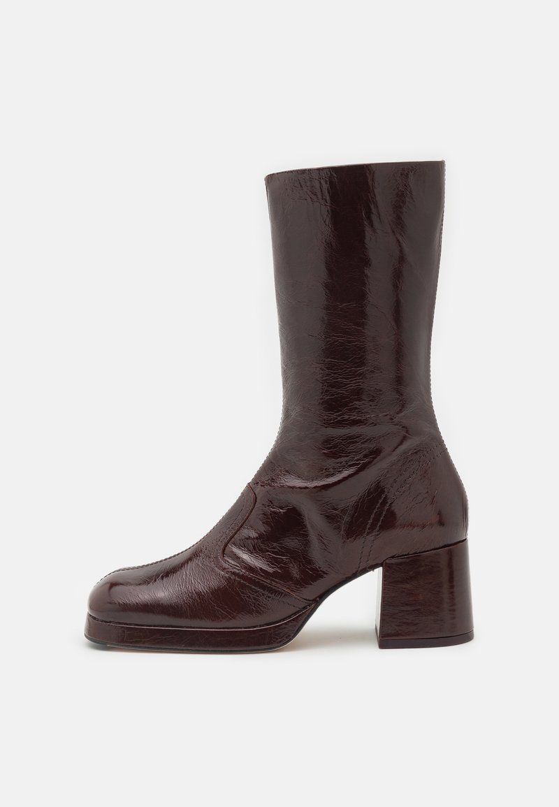 Botte en cuir marron foncé brillant, mi-mollet, avec bout rond et talon bloc sur fond blanc.