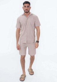 Chemise à manches courtes marron clair avec col et poche, associée à un short assorti. Fabriquée en matériau texturé et complétée par des sandales pratiques.