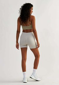 Shorts gris clair et un soutien-gorge de sport beige, caractérisés par un tissu doux, une coupe ajustée et des bretelles croisées dans le dos, associés à des baskets blanches.