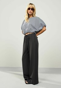 Sort højtaljede bredbenede bukser, der er parret med en cropped stribet skjorte i nuancer af hvid og marineblå. Tilbehøret inkluderer mørke solbriller.