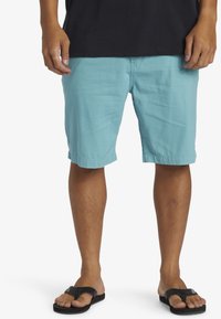 Turkosa shorts i lätt material med en avslappnad passform, sidofickor och uppvikta fållar. I kombination med svarta flip-flops.