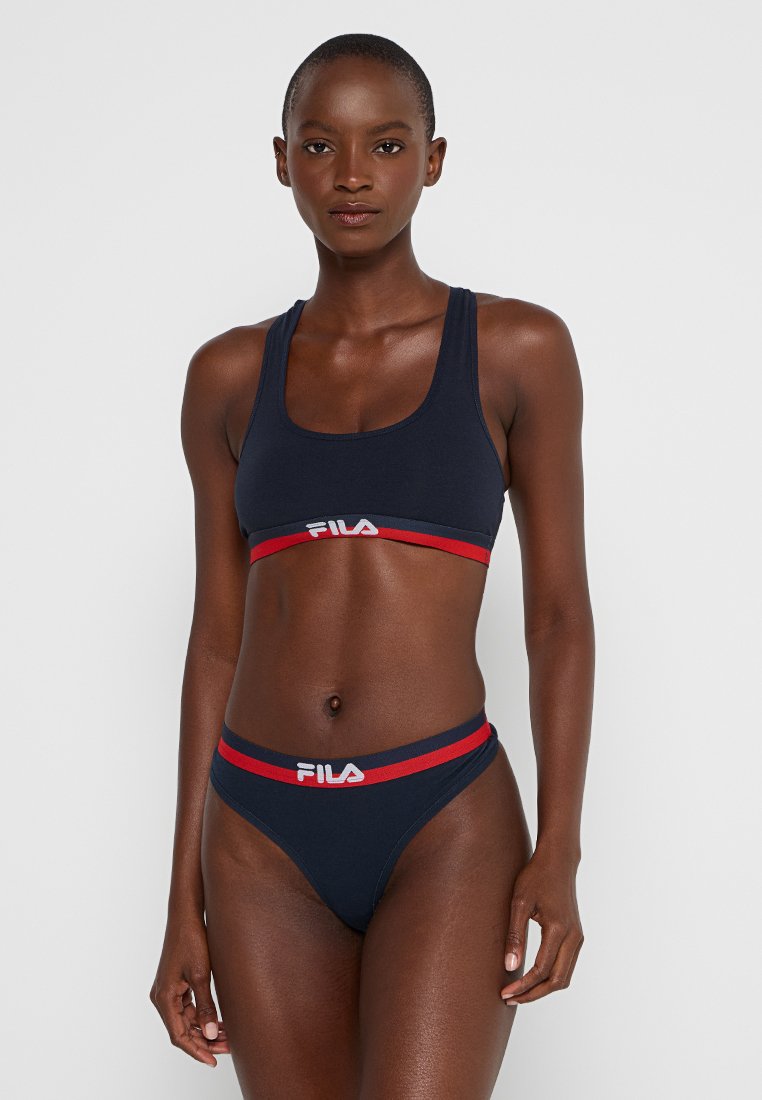 Ensemble de bralette sportive marine et string avec des marquages en rouge et blanc de FILA. Comprend des bandes élastiques et un matériau lisse et extensible.