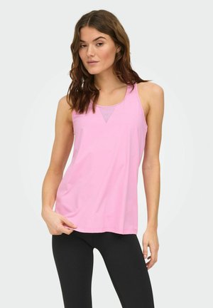 Kvinde iført en ærmeløs pink atletik tanktop og sorte leggings, stående mod en ensartet lys baggrund.