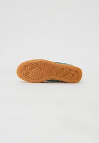 Schuhsohle mit strukturiertem Gummimuster und griffigem Profil. Farbe: orange mit sichtbarem, rundem Logo. Hintergrund ist einfarbig weiß.
