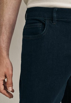 Tummat farkut slim fit -mallissa, joissa on hienovarainen rakenne, viisi taskua ja kontrastivärinen ommel vyötäröllä ja taskuissa.