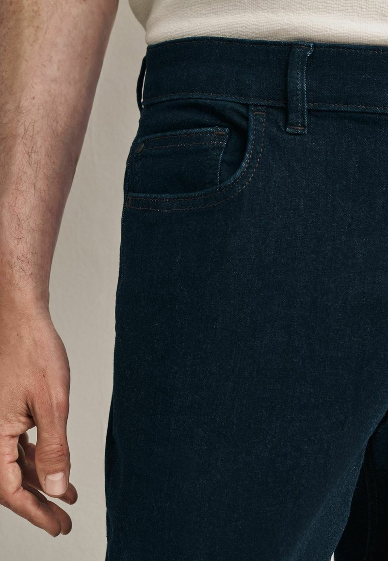 Tumedad denim teksad kitsas lõikega, peene tekstuuriga, viie tasku disainiga ning kontrastõmblustega vöökoha ja taskute juures.