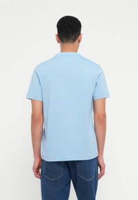 Tricou polo din bumbac de culoare albastră deschisă, cu guler scurt, mâneci scurte și croială dreaptă, având o textură netedă și un design minimalistic.