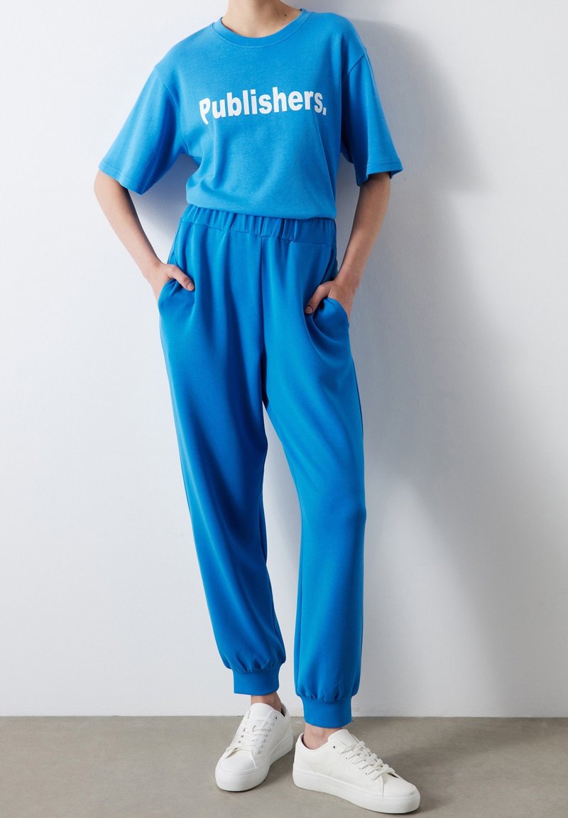 Bright blue two-piece outfit featuring a short-sleeve t-shirt with "Publishers." in white text, and matching elastic-waist jogger pants.