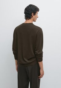 Brauner Strickpullover mit langen Ärmeln und einem gerippten Saum, getragen zu passenden dunklen Hosen. Die Rückseite zeigt einen klaren Halsausschnitt und eine leichte Textur.