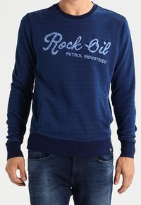 Námořnicky modré mikina s dlouhými rukávy, žebrovaným kulatým výstřihem a texturovaným logem "Rock Oil Petrol Industries" ve světle modré barvě.