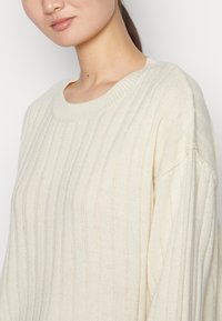 Maglione lavorato a maglia color crema con una trama a coste. Presenta un collo rotondo e spalle scese per una vestibilità comoda.