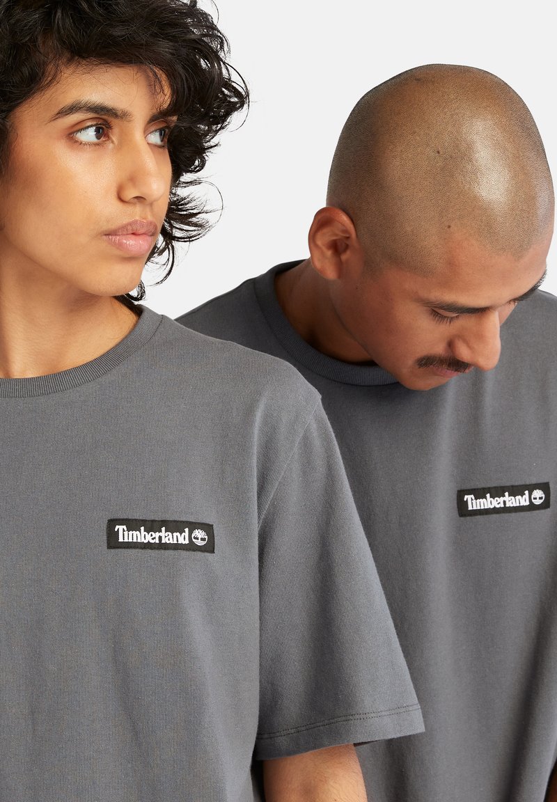 T-shirt grigie in cotone a maniche corte e scollatura tonda, con un'applicazione del logo nero Timberland sul petto, texture morbida.
